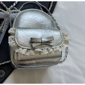 Detail of silver metallic mini backpack charm with white lace and bow decoration