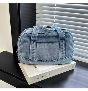 Detail shot of blue denim pillow bag with top handles and front pocket on book
