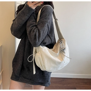 Detail of white large hobo bag with adjustable strap and heart wing charm on model