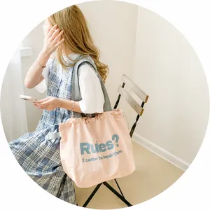 Pink canvas tote bag detail showing drawstring pleats and printed slogan on shoulder strap