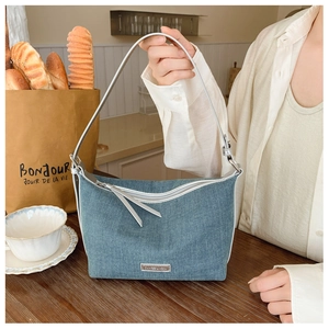 Dettaglio borsa hobo in denim blu con manici in pelle e targhetta in metallo