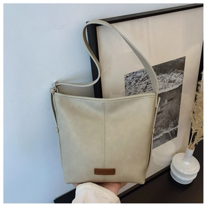 Detailed view of cream bucket bag with vertical stitching and brown leather logo tag