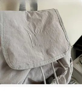 Close-up of light gray nylon backpack featuring embroidered logo and drawstring closure