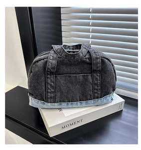 Detail of washed denim handbag showing mixed black and blue fabric with exterior pocket