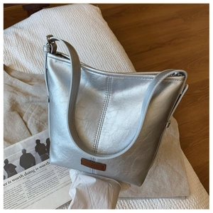 Close-up of a silver metallic shoulder bag featuring a brown leather brand logo patch