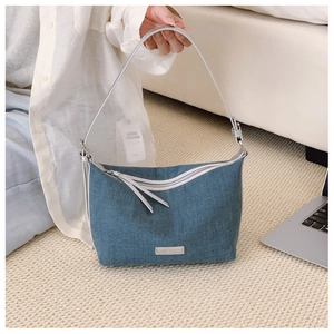 Dettaglio borsa a tracolla in denim blu con cinturino argento e targhetta in metallo