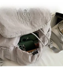 Detail of light gray nylon backpack showing drawstring side pocket for phone storage
