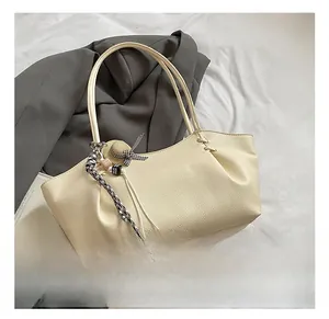 Detail view of beige tote bag with litchi texture leather and decorative ribbon charm