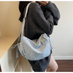 Detail of light blue crossbody bag featuring silver heart charm and woven rope accents