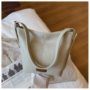Detail shot of a cream-colored bucket bag with leather texture and brand label on white pillow