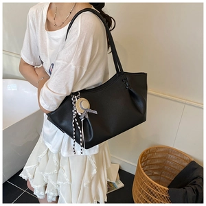 Detail of black pebbled leather tote with drawstring sides and straw hat ribbon charm
