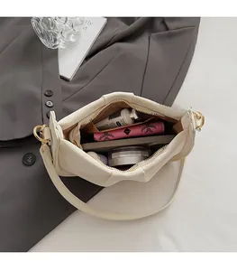 Vue macro des compartiments internes du sac plissé crème avec des objets du quotidien