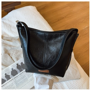 Detail of black lychee grain leather bucket bag featuring a brown brand logo plaque