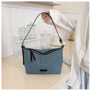 Dettaglio della borsa hobo in denim azzurro con manici in pelle nera e cerniere in metallo