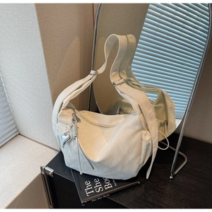 Detail of white large dumpling bag featuring silver heart charm and side drawstring pocket