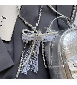Detail of silver embossed leather bag featuring a pearl lace bow and metal chain