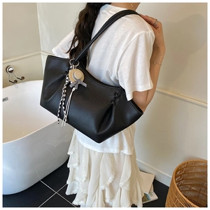 Detail of black pebbled leather tote with drawstring sides and bow hat charm on model