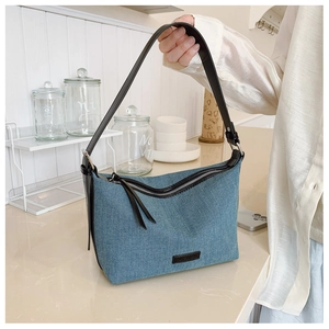 Dettaglio borsa a tracolla in denim blu con finiture in pelle nera e cerniera in metallo