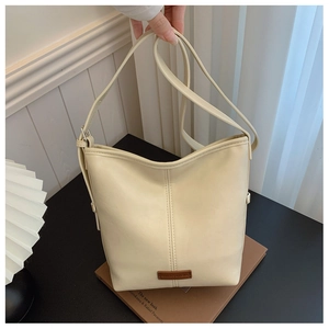 Detail of a creamy white leather bucket bag featuring a brown brand logo patch on the base