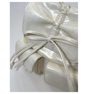 Detail of pearlescent white PU leather backpack with decorative bow and side pocket
