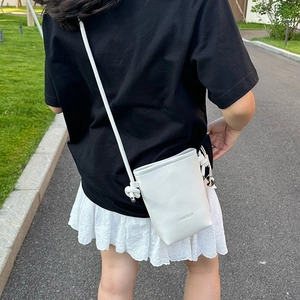 Détail du sac seau blanc en cuir grainé avec sangle nouée et breloque cloche argentée