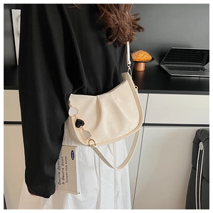 Détail du sac croissant crème avec design plissé et chaîne à breloques en cœur