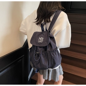 Detail of navy nylon backpack showing drawstring closure, MUTING logo and side pocket