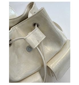 Close-up of creamy white drawstring backpack with glossy crinkled faux leather and metal eyelets