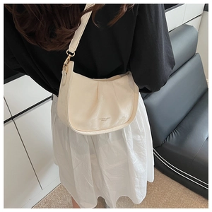 Détail du sac à bandoulière plissé crème avec boucles dorées porté par un mannequin