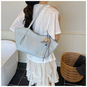 Close-up of light blue leather tote bag with straw hat pendant and ribbon decor