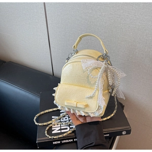 Détail d'un mini sac à dos jaune avec bordure en dentelle, nœud et chaîne perlée