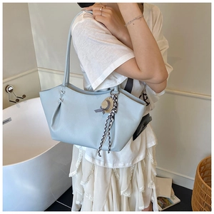 Detail of light blue leather tote bag with braided side accents and straw hat charm