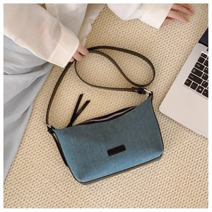Dettaglio borsa a dumpling in denim blu con tracolla in pelle e lunghe nappe