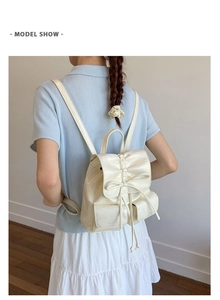 Detail of cream white leather backpack featuring decorative bow and drawstring closure