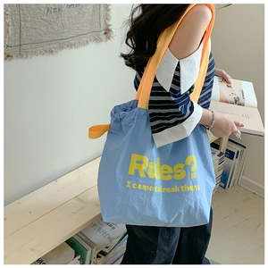 Close-up of light blue drawstring tote bag with vibrant orange straps and slogan detail