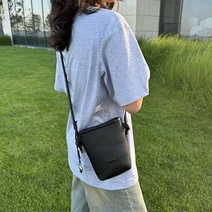 Détail d'un mini sac bandoulière en cuir grainé noir sur l'herbe verte à l'extérieur