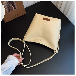 Detail of beige square crossbody bag with decorative stitching and leather logo plate