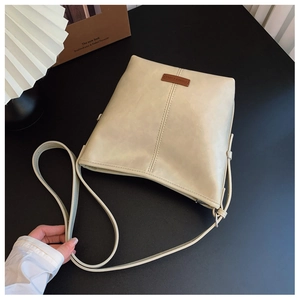 Detail of cream leather crossbody bucket bag with textured finish and brand logo tag