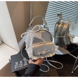 Détail du mini sac à dos argenté avec nœud en perles et finitions en dentelle blanche