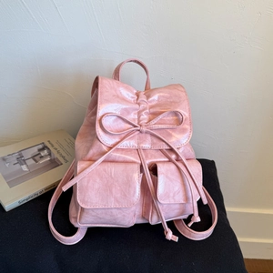 Detail view of pink glossy wrinkled leather backpack with bow drawstrings and utility pockets