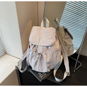 Detail of light gray nylon backpack showing drawstring closure and MUTING embroidery texture
