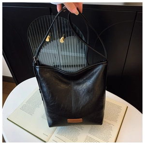 Detail of black bucket bag with a brown logo patch placed on a book over a white table