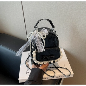 Gros plan d'un mini sac à dos noir en cuir avec nœud de perles et détails en dentelle