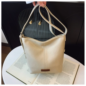 Detail of cream leather bucket bag with brand logo and adjustable strap on a book