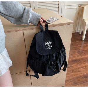 Detail of black nylon backpack with MUT ING embroidery hanging by a wooden cabinet