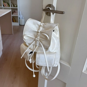 Detail of cream white leather backpack featuring bow tie design and glossy wrinkled texture