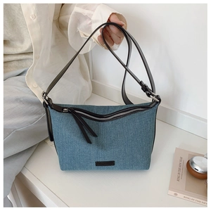 Dettaglio borsa hobo in denim blu con cerniera in pelle nera ed etichetta del marchio