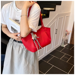 Detail of red pebbled leather tote bag with unique hat tassel charm and knotted shoulder strap