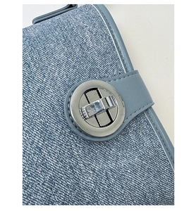 Detailed shot of a blue denim shoulder bag featuring a silver round rotating metal clasp