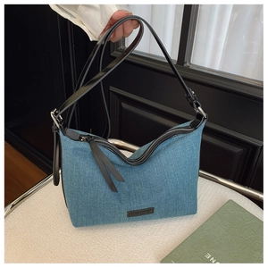Dettaglio borsa hobo in denim blu con logo in pelle e tracolla nera su sfondo minimalista